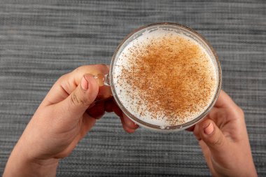A woman's hand is holding a white cup of hot milk drink with cinnamon called Turkish salep (sahlep).