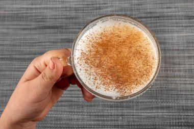 A woman's hand is holding a white cup of hot milk drink with cinnamon called Turkish salep (sahlep).