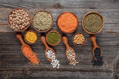 Vegan protein source.Various assortment of legumes, lentils, chickpea and beans assortment in different bowls on wooden table. Top view.