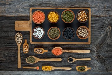 Vegan protein source.Various assortment of legumes, lentils, chickpea and beans assortment in different bowls on wooden table. Top view.