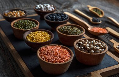 Vegan protein source.Various assortment of legumes, lentils, chickpea and beans assortment in different bowls on wooden table. Top view.