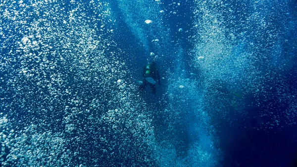 Artistic underwater photo of a scuba diver floating in a dream of air bubbles and rays of light in the deep blue ocean.