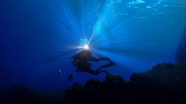 Scuba dalgıçlarının silueti güzel bir ışıkla koyu mavi denizde.