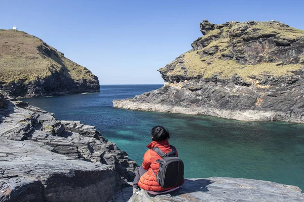 Kadın kayaların üzerinde oturuyor, arkası dönük ve önüne bakıyor. Cornwall, Boscastle, İngiltere 'de güzel okyanus manzarası.