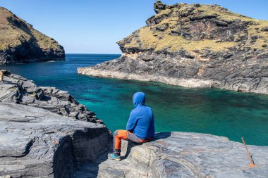 Adam arkasını yaslıyor ve önüne bakıyor. Cornwall, Boscastle, İngiltere 'de güzel okyanus manzarası.