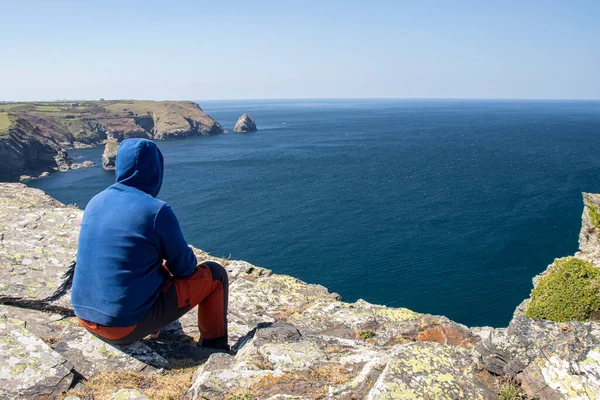 Adam arkasını yaslıyor ve önüne bakıyor. Cornwall, Boscastle, İngiltere 'de güzel okyanus manzarası.