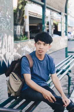 Otobüs durağında karalama dolu Asyalı bir adam bekliyor.