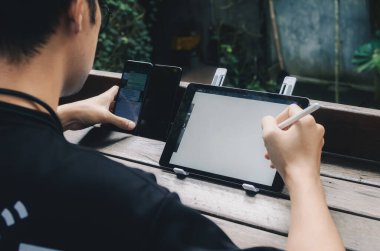 Genç yaratıcı tasarımcı parkta otururken dijital tablet ekranında stilus kalem çizimi yapıyor..