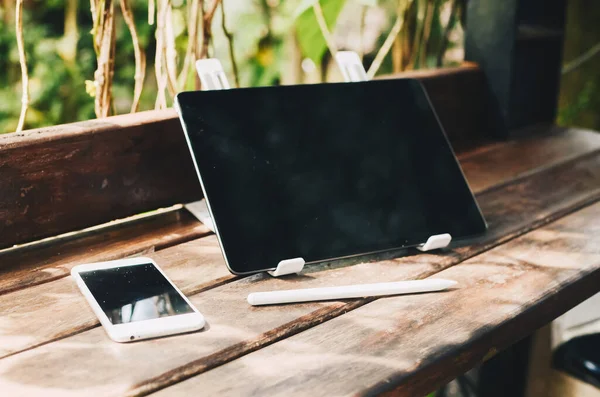 Tablet bilgisayar ve stilus tükenmez kalem dışarıda, tahta masada.