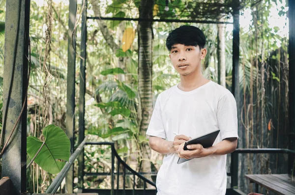 Asian man writing on tablet on nature background