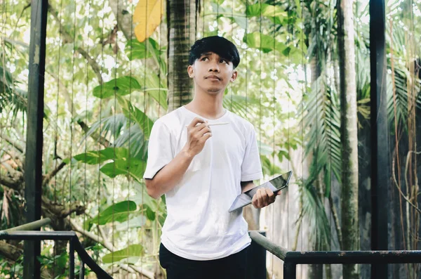 Asyalı adam düşünüyor ve doğanın geçmişi hakkında tablet tutuyor.