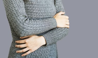 Uzun, sıcak, gri hırkalı genç bir kız, ısınıyor, mutlu ve pozitif, gri bir arkaplanda kendine güveniyor. Diğer dirseğini tutan bir kadının çapraz kolları, kendini beğenmişlik ve özgüven.