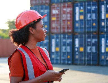 Bir çalışanın portresi ya da yönetici gülümseyen Afro-Amerikan kadın konteynır işçisi akıllı telefon kullanıyor. Sanayi malları, lojistik, ithalat-ihracat kavramı, başarısı ve hareketi.