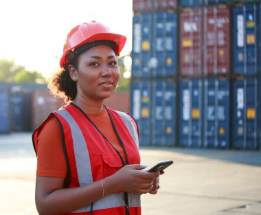 Bir çalışanın portresi ya da yönetici gülümseyen Afro-Amerikan kadın konteynır işçisi akıllı telefon kullanıyor. Sanayi malları, lojistik, ithalat-ihracat kavramı, başarısı ve hareketi.