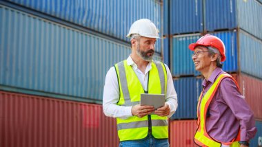 Kafkasyalı ve Asyalı işçiler takım çalışmacıları güvenli kıyafetler giyerler. Sert şapkalı iş kıyafetleri ve konteynır, konsept, depo, ithalat, ihracat, lojistik sektörü hizmetlerini denetlemek için bir tablet kullanın