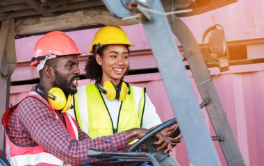 Depoda çalışan Afro-Amerikalı üniformalı kadın ve erkekler forklift kullanarak limandaki bir konteynırı kaldırıyor ve iş çıkartıyorlar. Konsept, takım, ticari nakliye. kargo ithalat-ihracatı