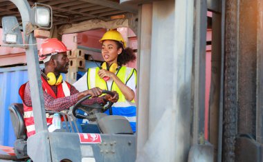 Depoda çalışan Afro-Amerikalı üniformalı kadın ve erkekler forklift kullanarak limandaki bir konteynırı kaldırıyor ve iş çıkartıyorlar. Konsept, takım, ticari nakliye. kargo ithalat-ihracatı