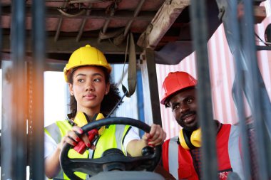 Depoda çalışan Afro-Amerikalı üniformalı kadın ve erkekler forklift kullanarak limandaki bir konteynırı kaldırıyor ve iş çıkartıyorlar. Konsept, takım, ticari nakliye. kargo ithalat-ihracatı