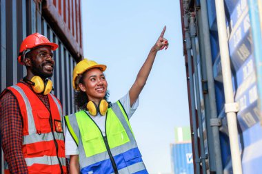Bir kadın mühendis ve genç bir Afro-Amerikan erkek ticari bir nakliye limanındaki konteynırların yüklenmesini denetliyor ve denetliyor. Takım çalışması kavramını kullanmaktan mutluluk duyarım. İthalat-ihracat-ithalat