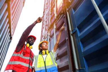 Bir kadın mühendis ve genç bir Afro-Amerikan erkek ticari bir nakliye limanındaki konteynırların yüklenmesini denetliyor ve denetliyor. Takım çalışması kavramını kullanmaktan mutluluk duyarım. İthalat-ihracat-ithalat