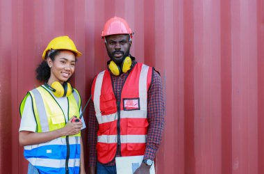 Bir kadın mühendis ve genç bir Afro-Amerikan erkek ticari bir nakliye limanındaki konteynırların yüklenmesini denetliyor ve denetliyor. Takım çalışması kavramını kullanmaktan mutluluk duyarım. İthalat-ihracat-ithalat