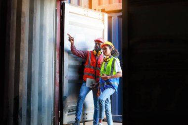 Bir kadın mühendis ve genç bir Afro-Amerikan erkek ticari bir nakliye limanındaki konteynırların yüklenmesini denetliyor ve denetliyor. Takım çalışması kavramını kullanmaktan mutluluk duyarım. İthalat-ihracat-ithalat