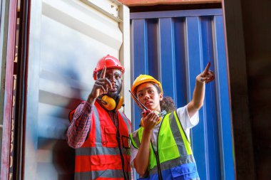 Bir kadın mühendis ve genç bir Afro-Amerikan erkek ticari bir nakliye limanındaki konteynırların yüklenmesini denetliyor ve denetliyor. Takım çalışması kavramını kullanmaktan mutluluk duyarım. İthalat-ihracat-ithalat