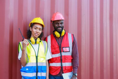 Bir kadın mühendis ve genç bir Afro-Amerikan erkek ticari bir nakliye limanındaki konteynırların yüklenmesini denetliyor ve denetliyor. Takım çalışması kavramını kullanmaktan mutluluk duyarım. İthalat-ihracat-ithalat