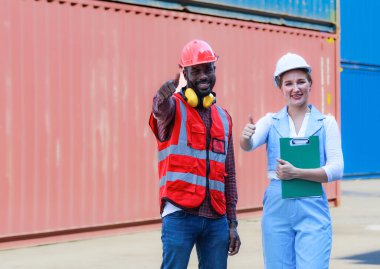 Afrika kökenli Amerikalı erkekler ve beyaz kadınlar kask takıyor, gülümsüyor, konuşuyor, belgeleri tutuyor, konteynır, konsept, depolama, ithalat, ihracat, lojistik sektörü hizmetlerini denetlemeye çalışıyorlar..