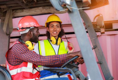 Depoda çalışan Afro-Amerikalı üniformalı kadın ve erkekler forklift kullanarak limandaki bir konteynırı kaldırıyor ve iş çıkartıyorlar. Konsept, takım, ticari nakliye. kargo ithalat-ihracatı
