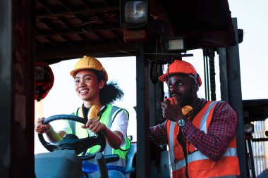 Depoda çalışan Afro-Amerikalı üniformalı kadın ve erkekler forklift kullanarak limandaki bir konteynırı kaldırıyor ve iş çıkartıyorlar. Konsept, takım, ticari nakliye. kargo ithalat-ihracatı