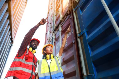 Bir kadın mühendis ve genç bir Afro-Amerikan erkek ticari bir nakliye limanındaki konteynırların yüklenmesini denetliyor ve denetliyor. Takım çalışması kavramını kullanmaktan mutluluk duyarım. İthalat-ihracat-ithalat