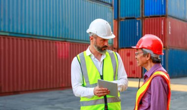 Kafkasyalı ve Asyalı işçiler takım çalışmacıları güvenli kıyafetler giyerler. Sert şapkalı iş kıyafetleri ve konteynır, konsept, depo, ithalat, ihracat, lojistik sektörü hizmetlerini denetlemek için bir tablet kullanın