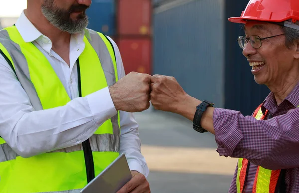 Beyaz ve Asyalı bir takım, güvenlik önlemi alıyorlar. Sert şapkalı iş kıyafeti ve ilk çarpışma konteynır teftişi konsepti kullanarak ithalat-ihracat lojistik sektörü hizmeti