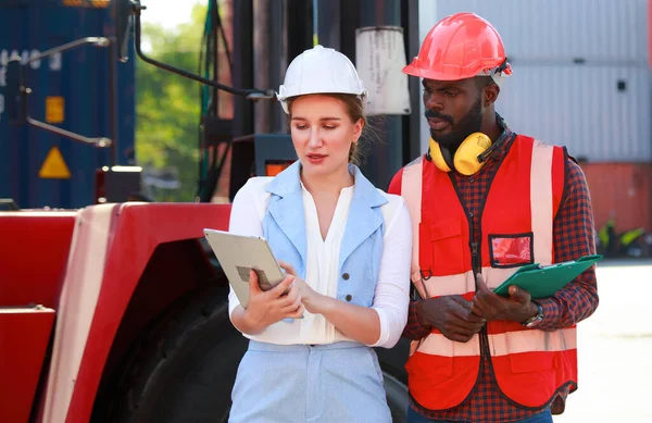 A young African-American engineer and Caucasian woman manager monitor and supervise the loading of containers at a commercial shipping port. happy using tablet concept import-export import-export