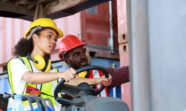 Depoda çalışan Afro-Amerikalı üniformalı kadın ve erkekler forklift kullanarak limandaki bir konteynırı kaldırıyor ve iş çıkartıyorlar. Konsept, takım, ticari nakliye. kargo ithalat-ihracatı