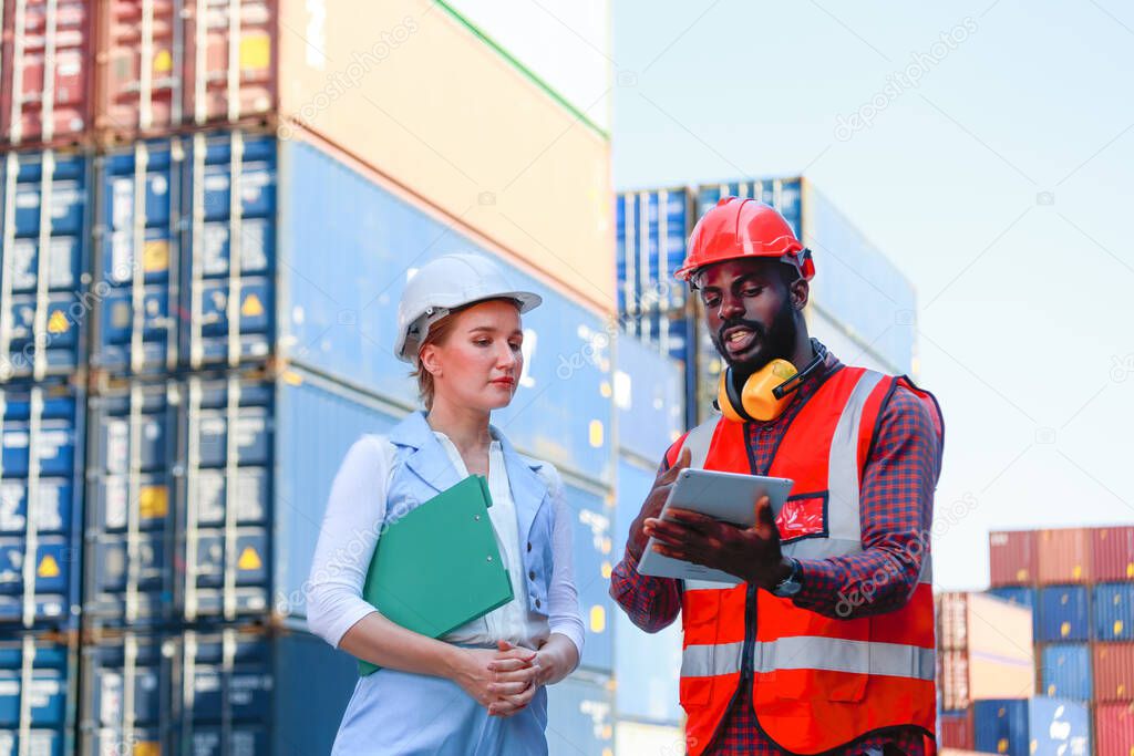 A young African-American engineer and Caucasian woman manager monitors and supervises the loading of containers at a commercial shipping port. happy using tablet concept import export import export