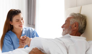 Genç doktor onunla ilgilenmek için yaşlı bir beyaz adamın elini tuttu. Yatak odasında yatarken hastalığından bahset. Sağlık, Yaşlılık, Sağlık ve Emeklilik Konsepti