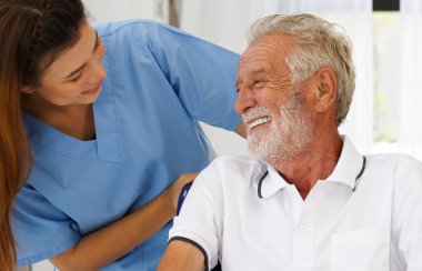A nursing nurse with a Caucasian senior man in a wheelchair looking out the window. Happy chatting in the hallway of the nursing home. health concept Help rehabilitate aging, medical and retirement.