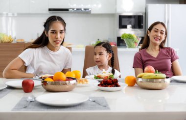 Mutlu bir Asyalı aile öğle yemeği, sebze, meyve ve tarihlerini evlerindeki masada geçirir. Tatlı küçük kız konuşuyor, eğleniyor. Anne, teyze. Mutlu aile ilişkileri konsepti. Yaşam biçimi.
