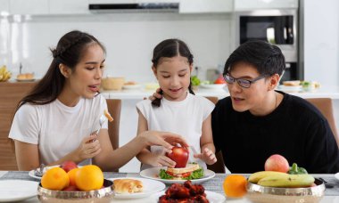 Mutlu bir Asyalı aile öğle yemeği, sebze, meyve ve tarihlerini evlerindeki masada geçirir. Tatlı küçük kız konuşuyor, eğleniyor. Baba, anne. Mutlu aile ilişkileri konsepti. Yaşam biçimi.