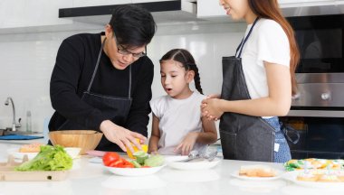 Mutfakta mutlu bir aile yemeği. Baba, anne ve tatlı küçük kız sebzeleri salata yapmak için dönüştürüyorlar. Evdeki mutfakta yemek hazırla. Mutlu aile ilişkisi konsepti Yaşam tarzı.