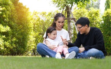 Asyalı ailenin parlak ve tatlı kızı, açık mavi gökyüzü çimlerinde ve yeşil ağaçlarda koşuşturarak rahatlıyor, anne ve babasının arkasında, onlara bakıyorlar. Mutlu aile ilişkisi konsepti, yaşam tarzı.
