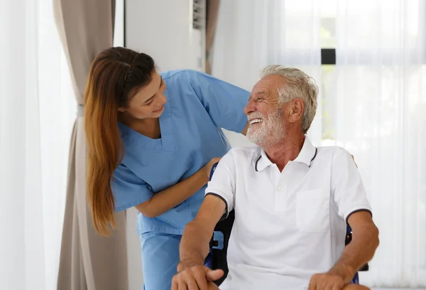 Tekerlekli sandalyedeki yaşlı beyaz bir adamla camdan bakan bir hemşire. Huzurevinin koridorunda iyi sohbetler. Sağlık konsepti yaşlanma, sağlık ve emekliliğin rehabilitasyonuna yardımcı olur.