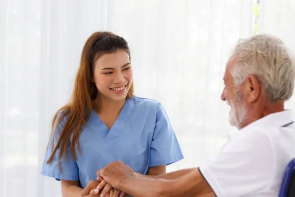 Kadın doktor, yaşlı beyaz erkek, yetişkin, hemşire koğuşu sağlık konseptinde tekerlekli sandalyedeki hasta ile konuşmayı teşvik etmek için el ele tutuşmaya yardım ediyor. Yaşlanmanın, tıbbi ve emekliliğin geri gelmesine yardımcı oluyor..