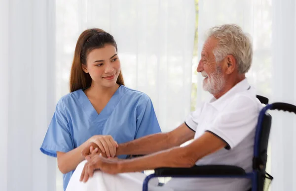 Kadın doktor, yaşlı beyaz erkek, yetişkin, hemşire koğuşu sağlık konseptinde tekerlekli sandalyedeki hasta ile konuşmayı teşvik etmek için el ele tutuşmaya yardım ediyor. Yaşlanmanın, tıbbi ve emekliliğin geri gelmesine yardımcı oluyor..
