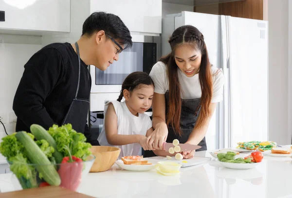 Mutfakta mutlu bir aile yemeği. Baba, anne ve tatlı küçük kız sebzeleri salata yapmak için dönüştürüyorlar. Evdeki mutfakta yemek hazırla. Mutlu aile ilişkisi konsepti Yaşam tarzı.