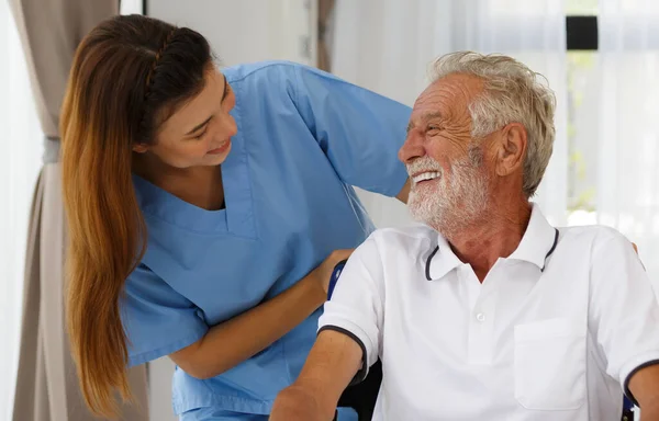 Tekerlekli sandalyedeki yaşlı beyaz bir adamla camdan bakan bir hemşire. Huzurevinin koridorunda iyi sohbetler. Sağlık konsepti yaşlanma, sağlık ve emekliliğin rehabilitasyonuna yardımcı olur.