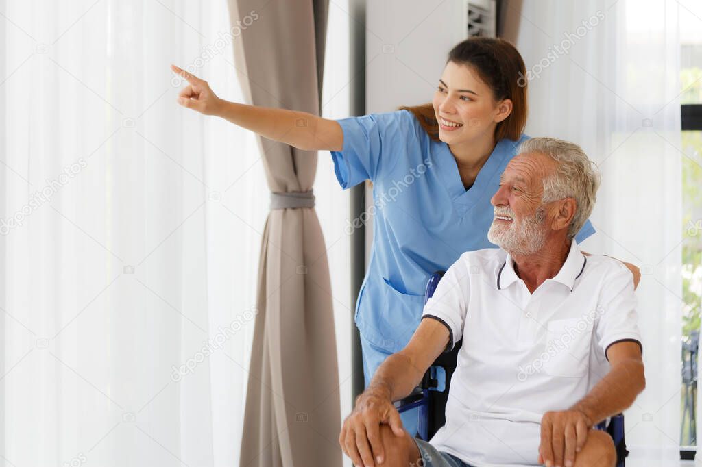 A nursing nurse with a Caucasian senior man in a wheelchair looking out the window. Happy chatting in the hallway of the nursing home. health concept Help rehabilitate aging, medical and retirement.