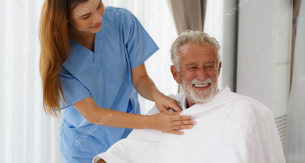 A female nurse uses a blanket on a senior Caucasian man sitting in a wheelchair, encouraging, talking, and helping to care for the elderly, concept, health, rehabilitation, medical, and retirement.